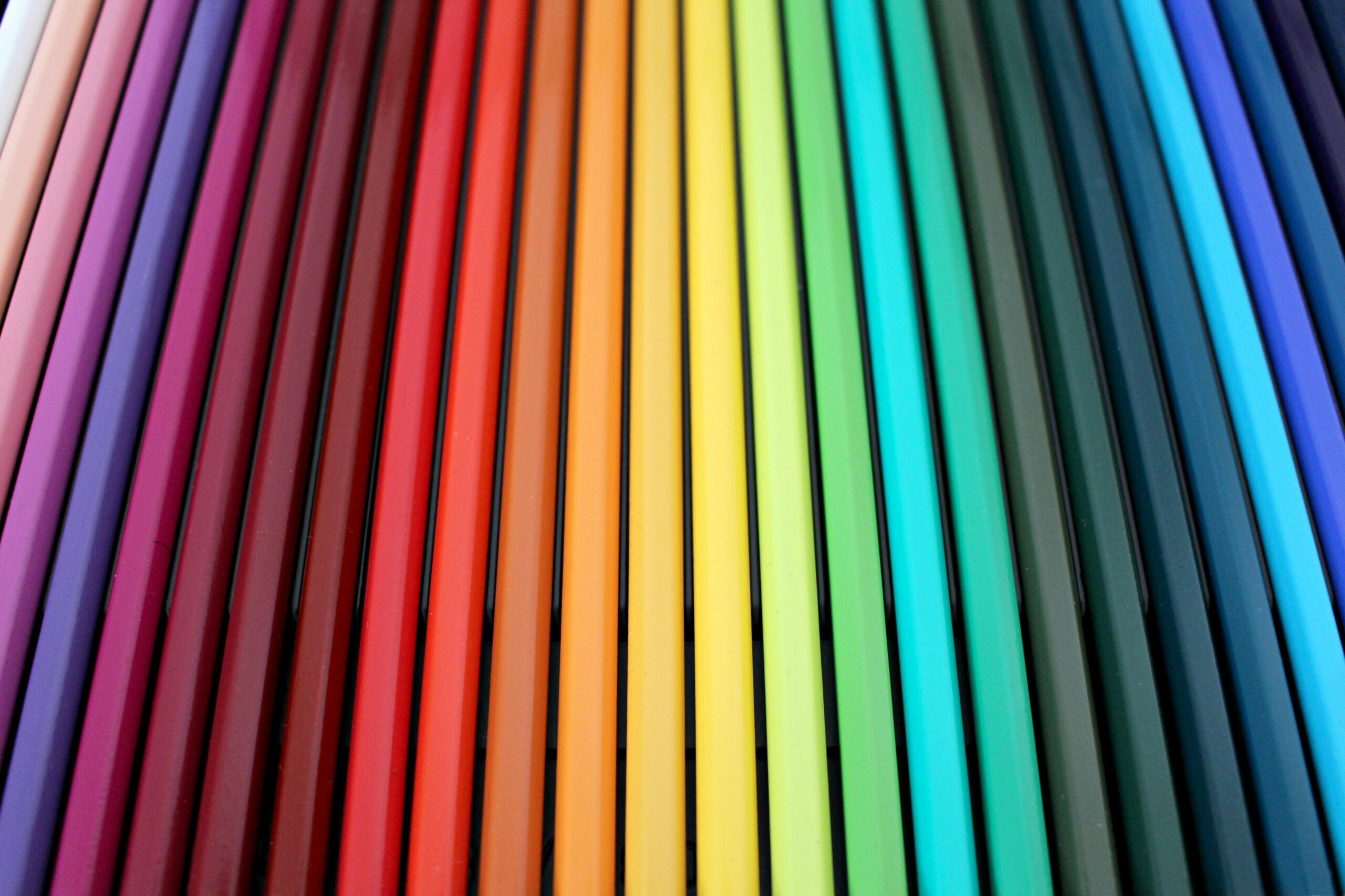 A vibrant and colorful arrangement of colored pencils forming a rainbow spectrum pattern.